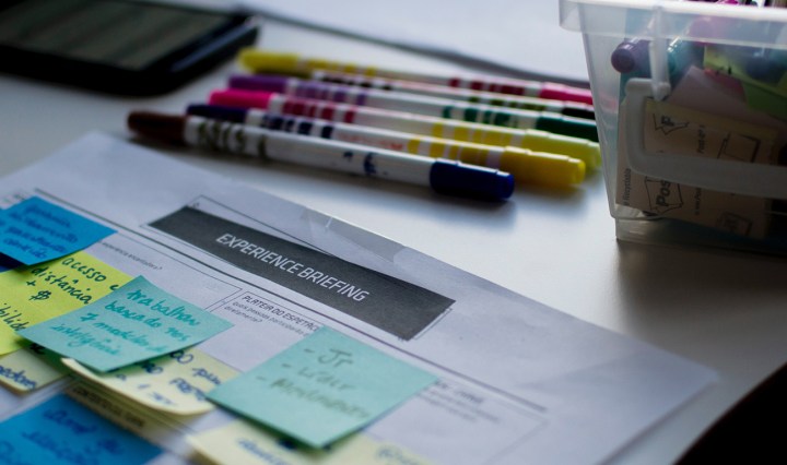 A piece of paper with lots of bright sticky notes,pens and textas in the background