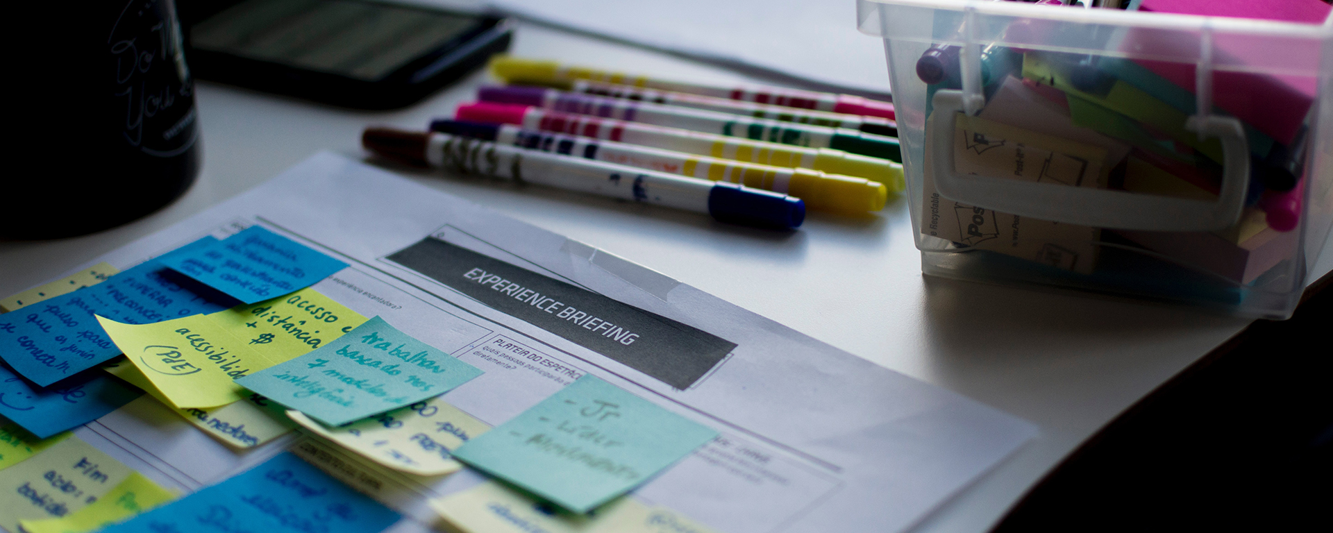 A piece of paper with lots of bright sticky notes,pens and textas in the background