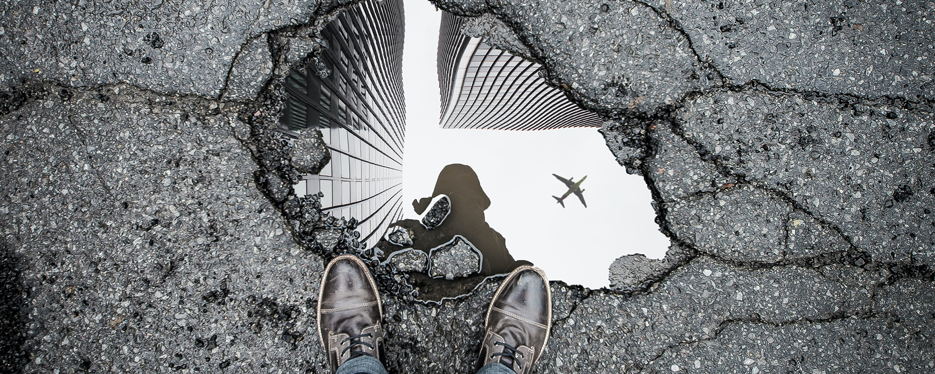 A person's shoes are shown from POV, standing over a puddle, where the person's outline is reflected