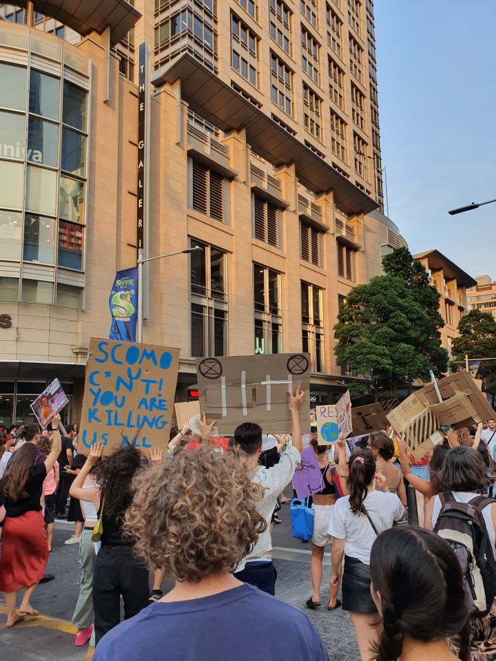 Protesters march in Sydney. Sign reads: Scomo, you cu*nt, you're killing us