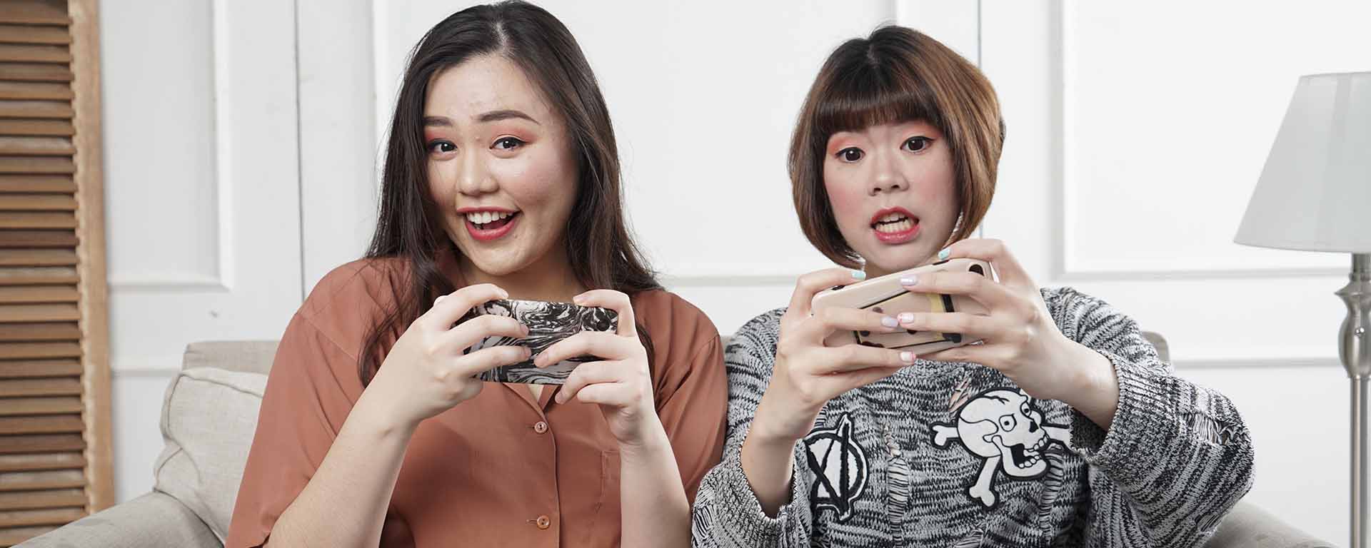 Two Asian women are playing a game on their mobile phones and they looked amused
