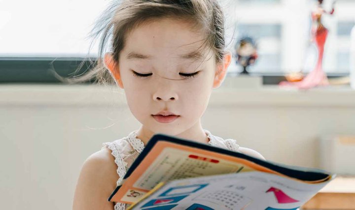 A young Asian girl is reading a magazine