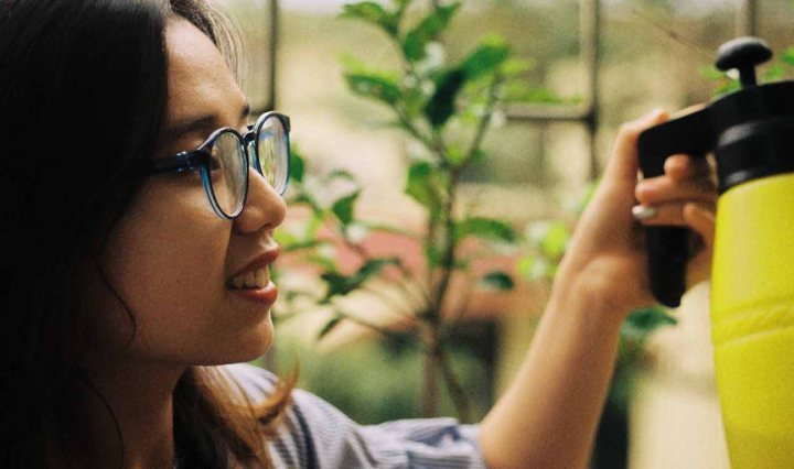 An Asian woman is smiling as she waters plants