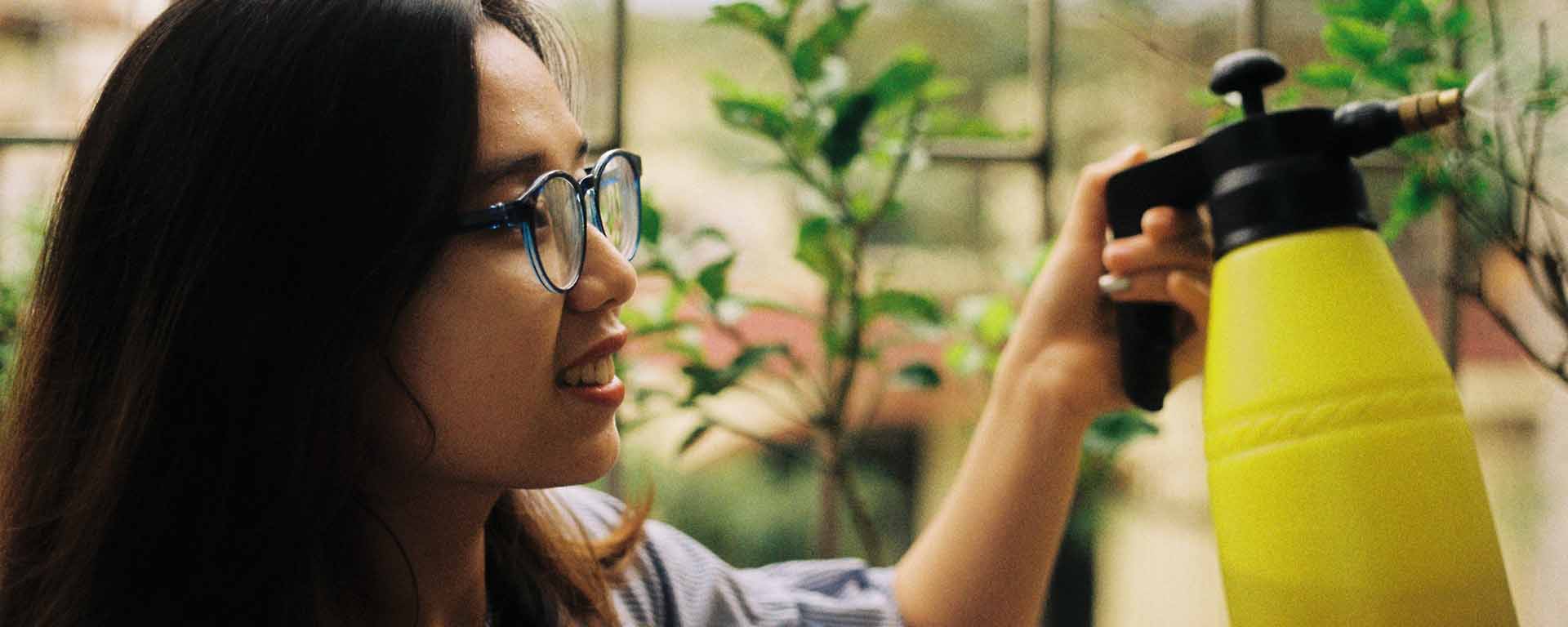 An Asian woman is smiling as she waters plants