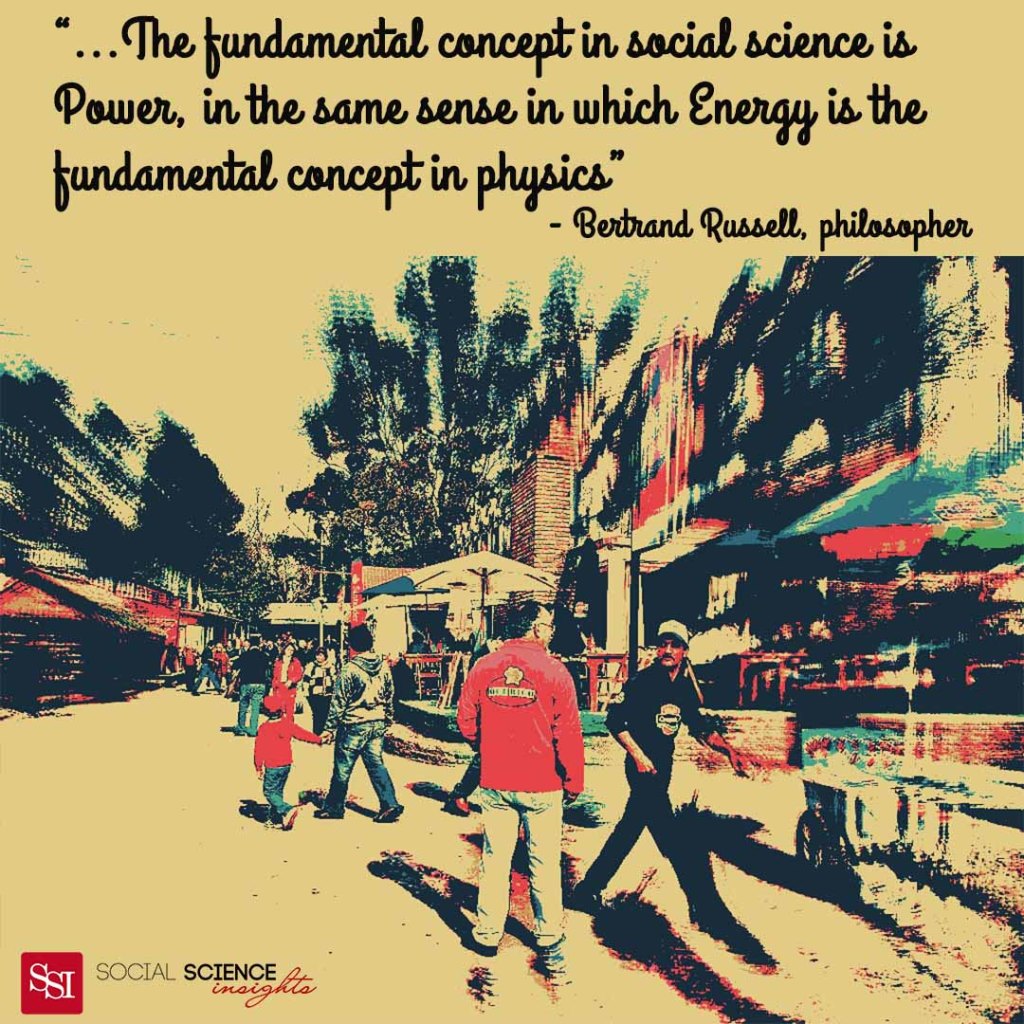 People walk down a busy street. A man is stationary, talking to a man who is walking away