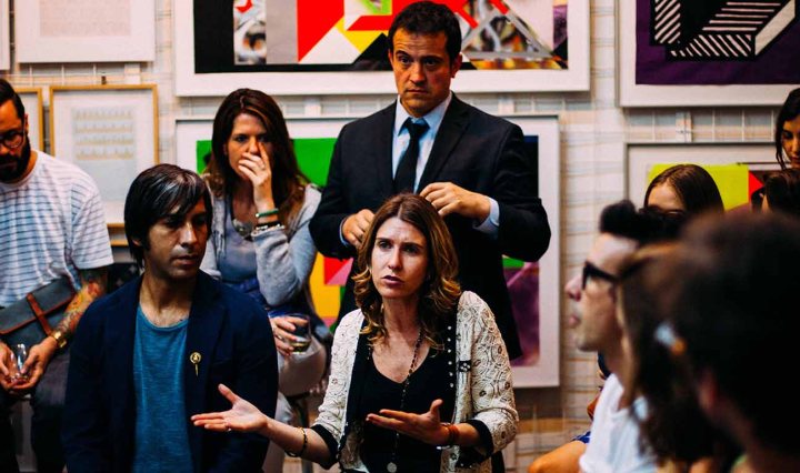 A room full of majority white people are listening to a woman speak about something seemingly serious