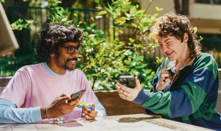 Two people outdoors smile as they look at their phones