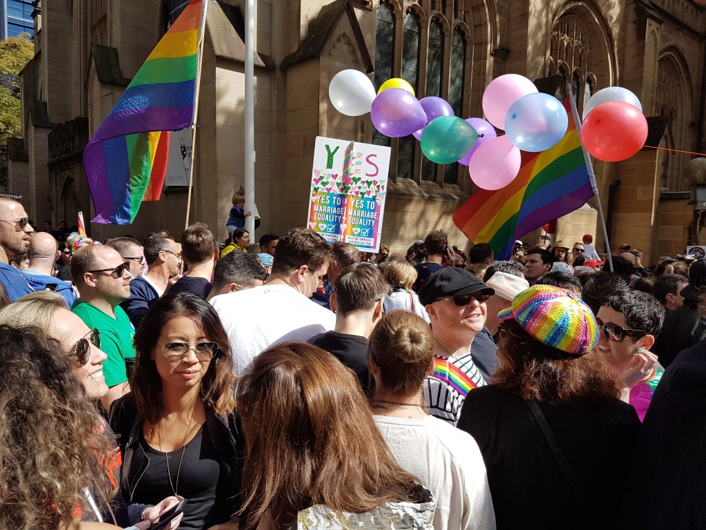 People hold balloons, the Pride Flag, and a sign saying "YES" at the Marriage Equality march in Sydney