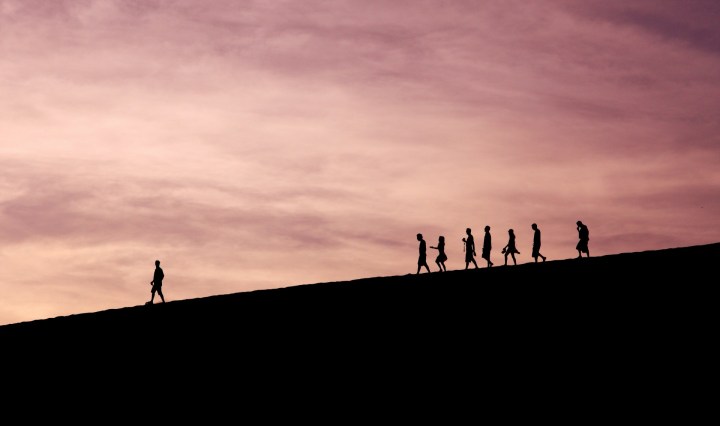 A silhouetted people walk down a hill, following one person in the lead