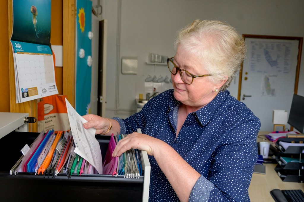 A woman with white hair looks at a file in an open filing cabinet