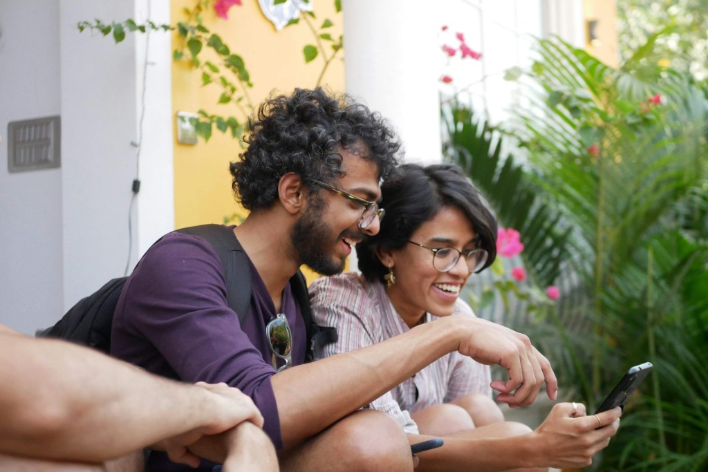 A man and woman sit outdoors, smiling as they look at the woman's mobile phone