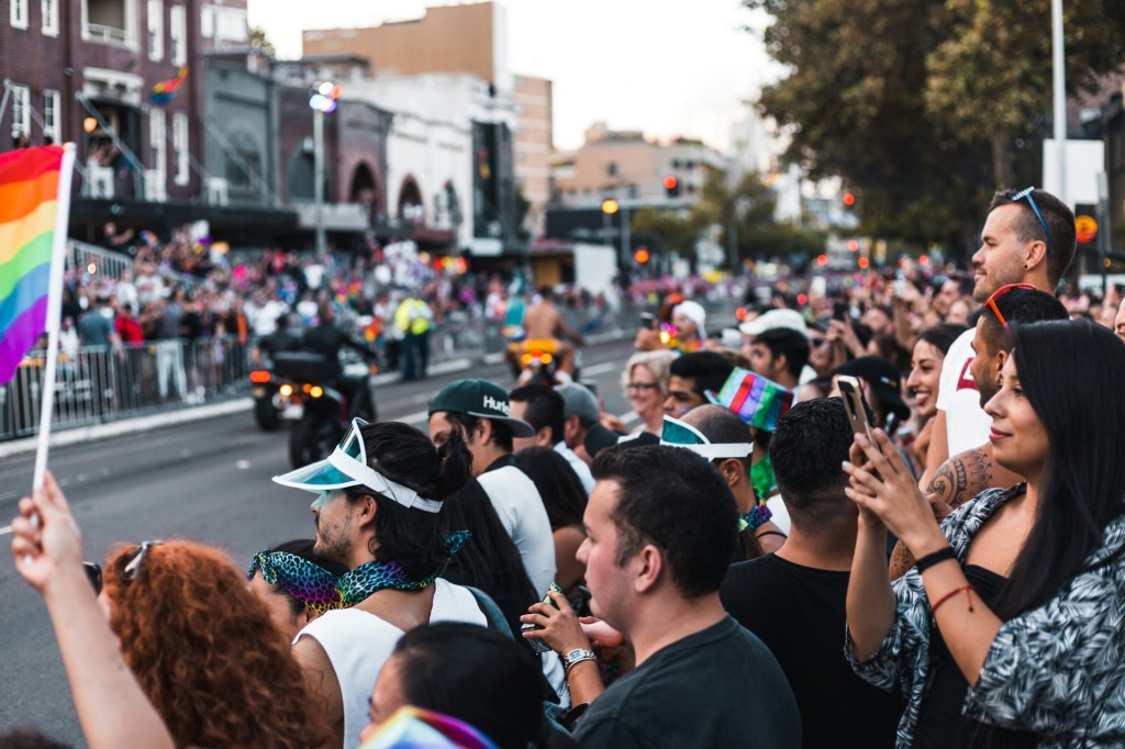 A crowd of people wave the pride flag and stand behind a barricade at the Sydney Mardi Gras