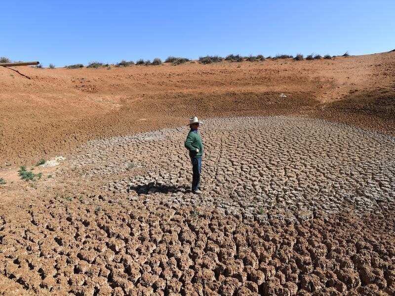 Man wearing a hat stands in a middle of a barren field in New South Wales