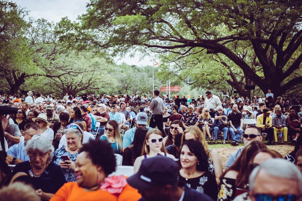 Crowd of diverse people sit outdoors on deck chairs under trees