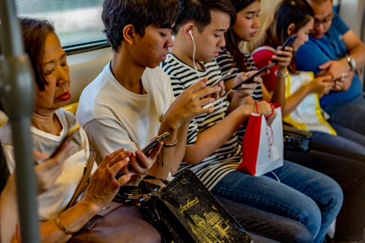 Asian people seated on public transport scroll and watch their phones