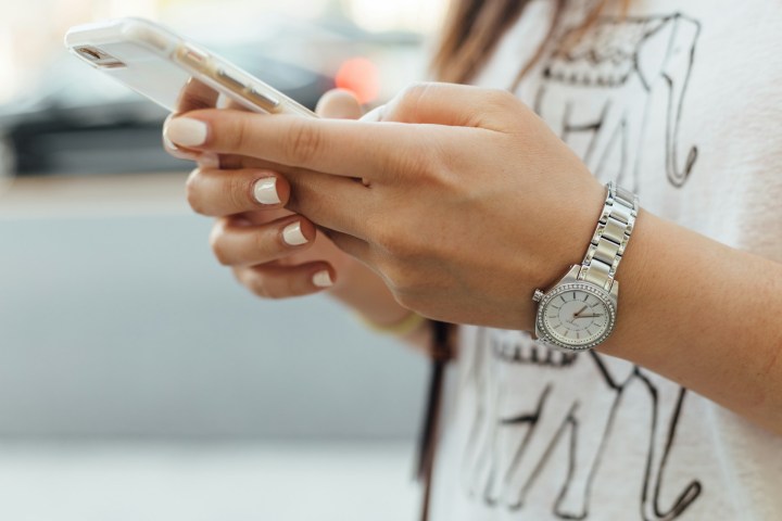 A white woman's hands holds a phone, with the thumb mid-scroll
