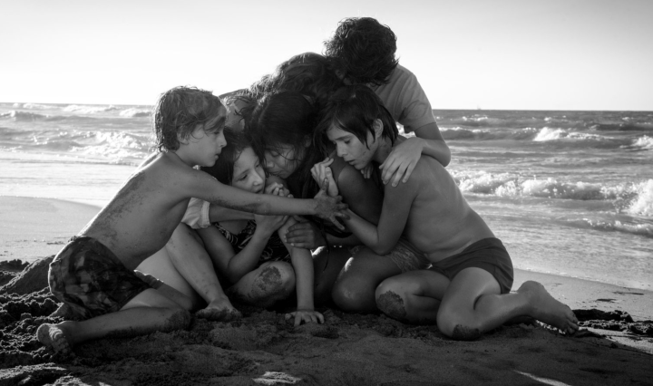 A a huddled group of children and a woman at the beach, in black and white