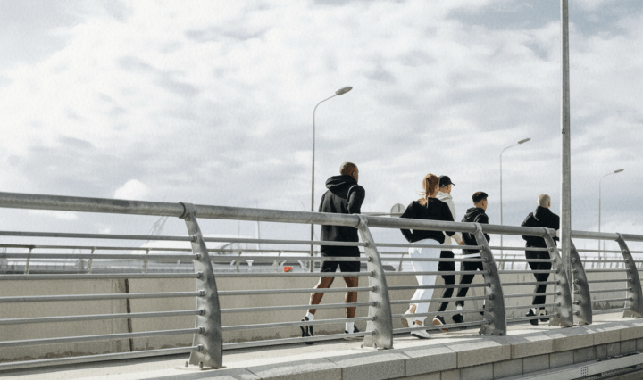 A group of five people run on a bridge against a stormy sky