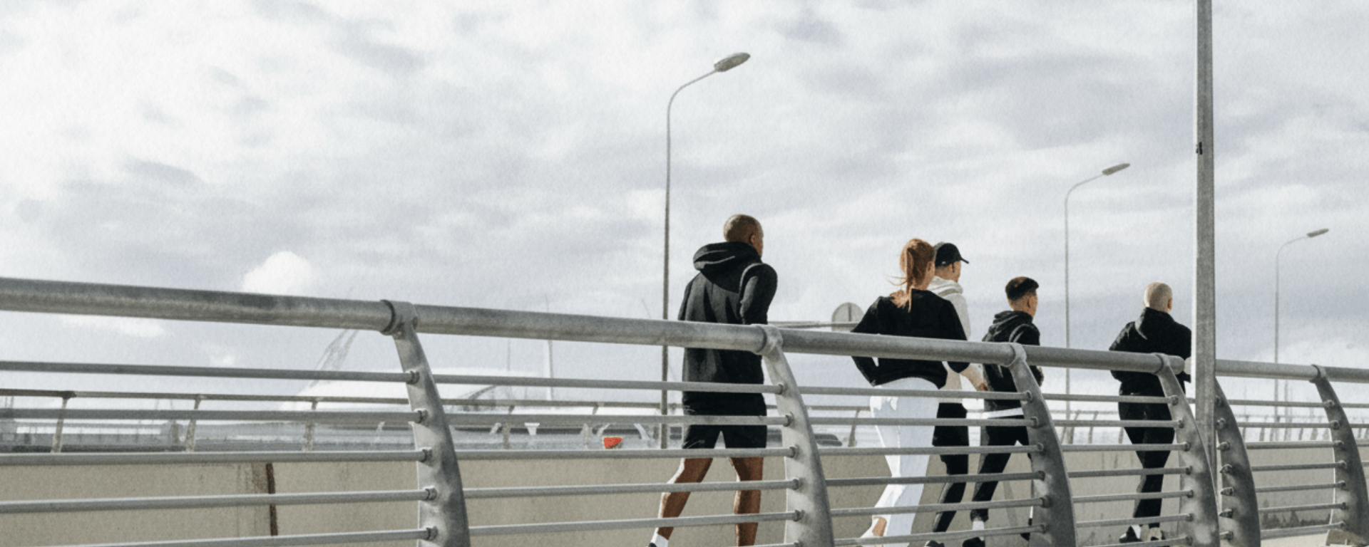 A group of five people run on a bridge against a stormy sky