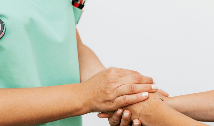 Torso of a health worker wearing a stethescope holding hands with a patient