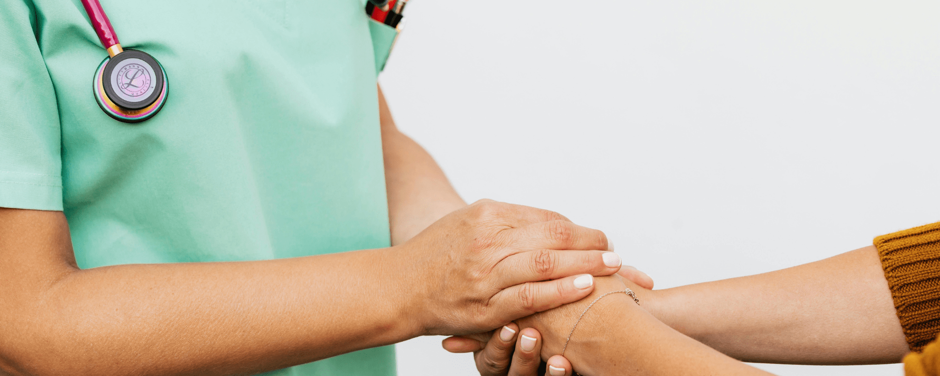 Torso of a health worker wearing a stethescope holding hands with a patient
