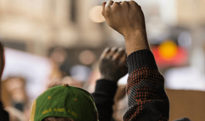 People of colour workers raise their fists in the air during a protest