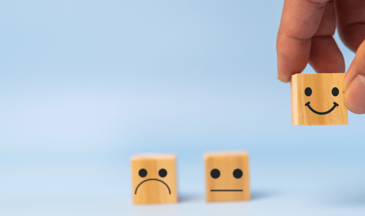 A hand picks up a block with a smiling face, leaving blocks with neutral and unhappy faces