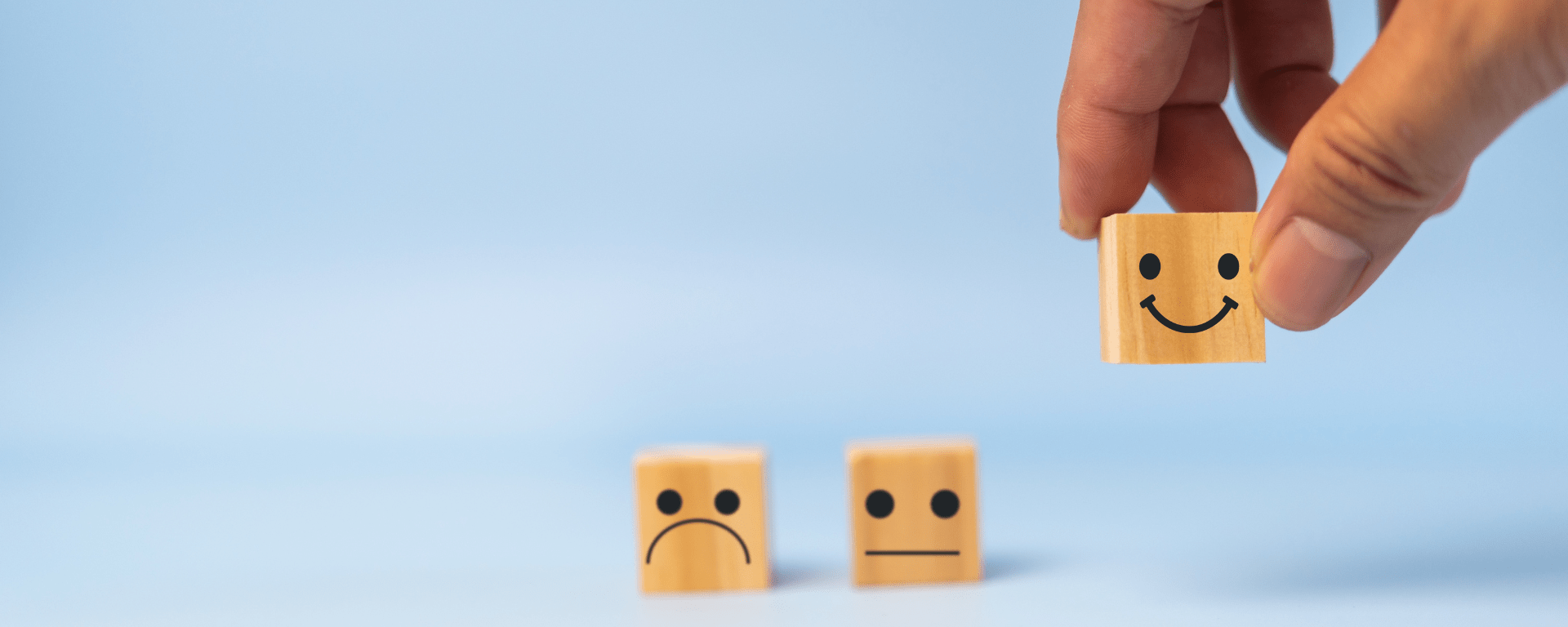 A hand picks up a block with a smiling face, leaving blocks with neutral and unhappy faces