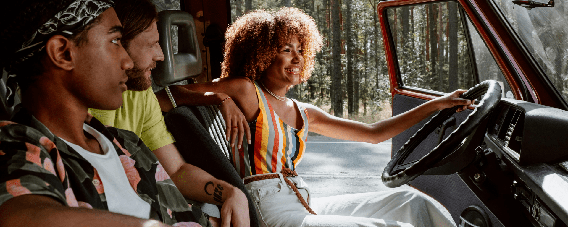 A smiling young Black woman sits with the driver's door open, while a Black man and white man look at her