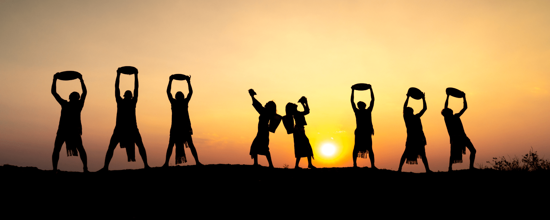 Vietnamese dancers silhouetted against the sunset. They hold up instruments and pose in triumph and celebration